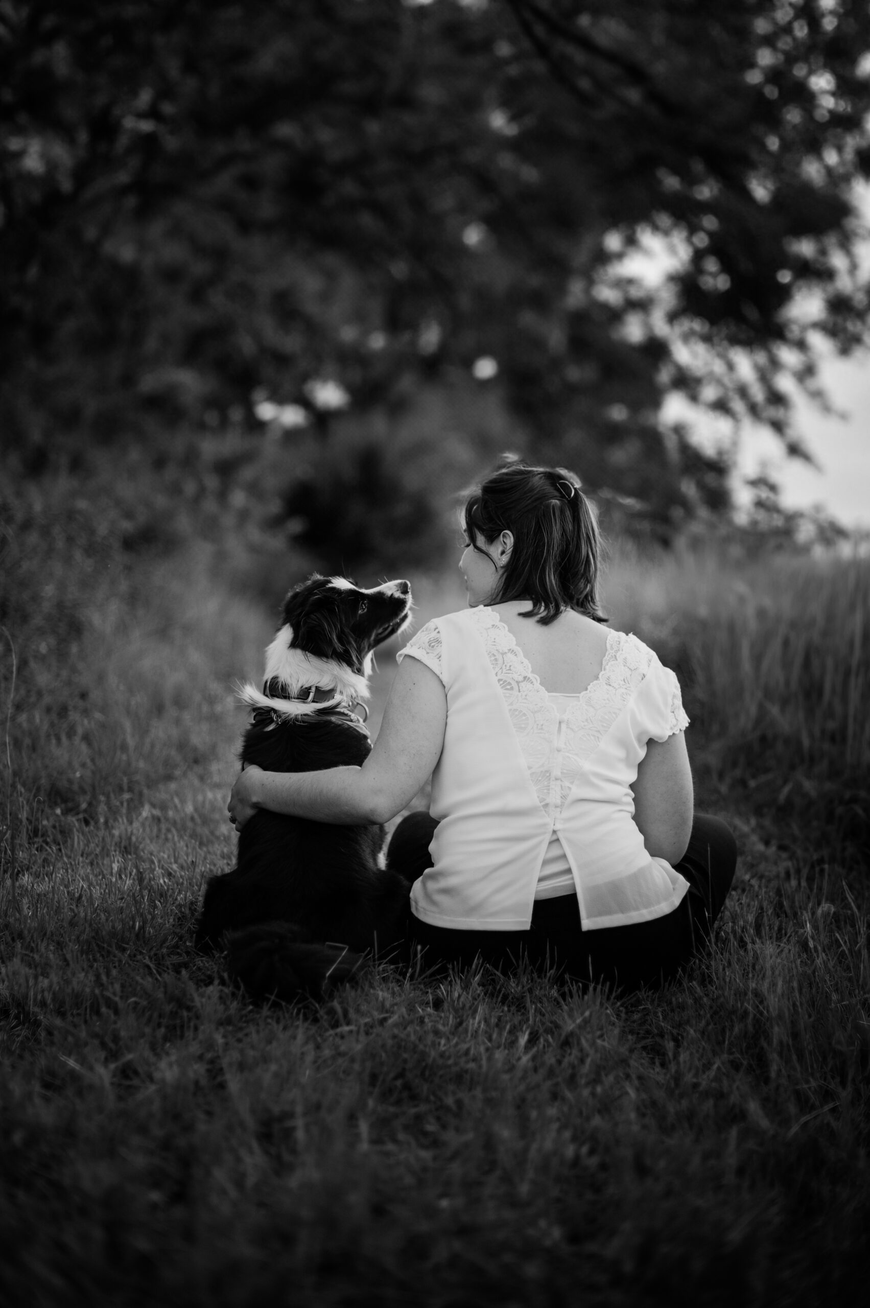 Photographe chien et maître Allier femme assise avec son border collie dans l'herbe noir et blanc
